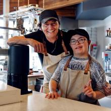 Smiling man and a person with a disability working behind the counter of a coffee shop