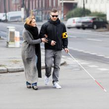 Woman assisting blind man with a cane walking across the street