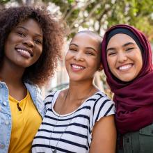 Gros plan de trois femmes formant un groupe multi-ethnique qui sourient à la caméra.