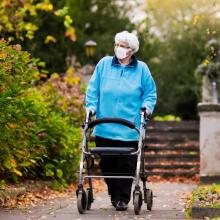 Elderly woman wearing a mask pushes her walker through a park 