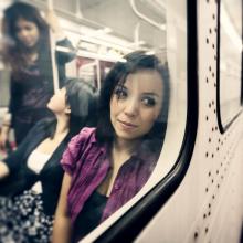 Pensive woman looking out the window of subway train as friends talk in background. Toronto
