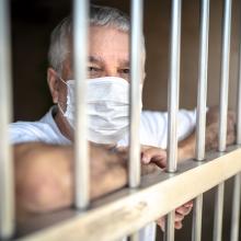 Prisoner behind bars wearing a protective mask